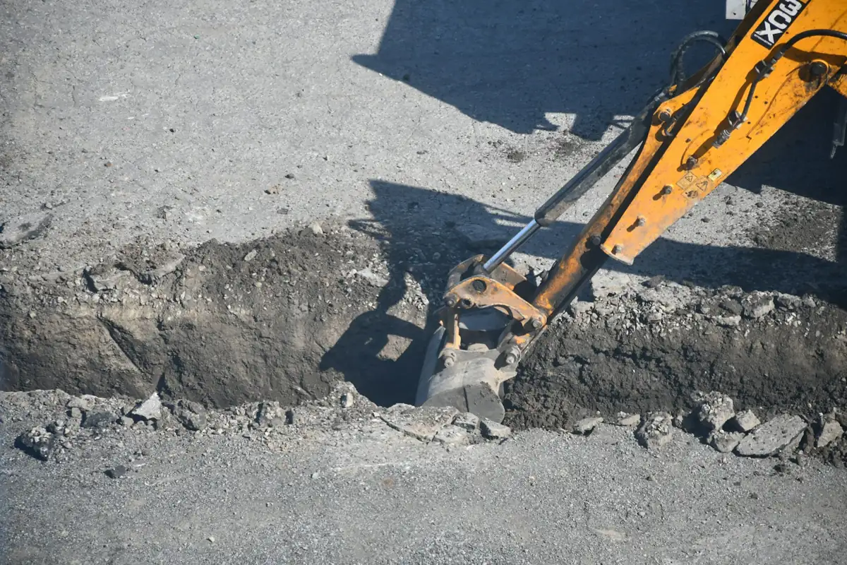Excavator bucket digging through road pavement, the kind of mechanical digging hydrovac replaces near utilities